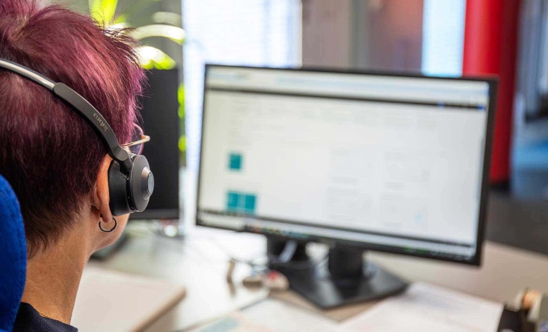 Computer-Bildschirm im Anschitt eine GWH-Mitarbeiterin mit Headset